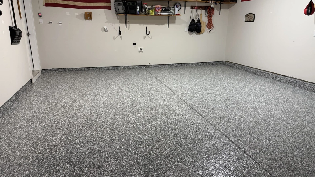 A garage with light gray walls and a newly installed gray epoxy flake floor, showing shelves and hooks.